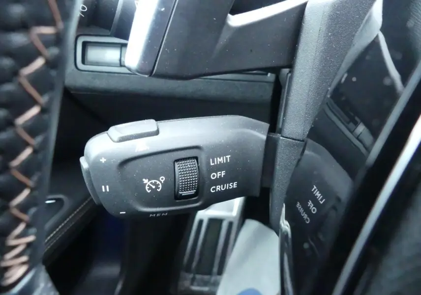 Gros plan sur la commande de régulateur de vitesse noire à gauche du volant cuir perforé du Peugeot 5008 GT noir métallisé 2023.