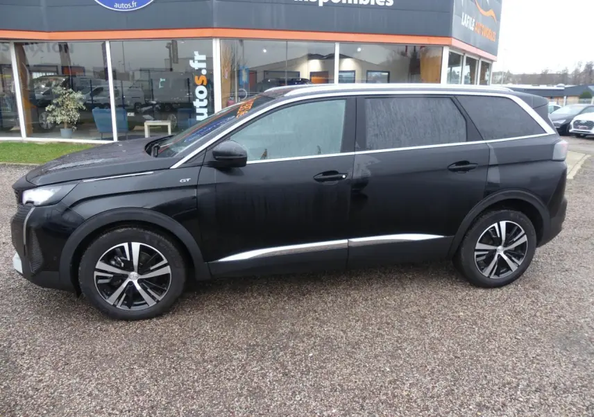 Profil droit d'un Peugeot 5008 GT 2023 noir métallisé avec jantes bi-ton et barres de toit en aluminium.