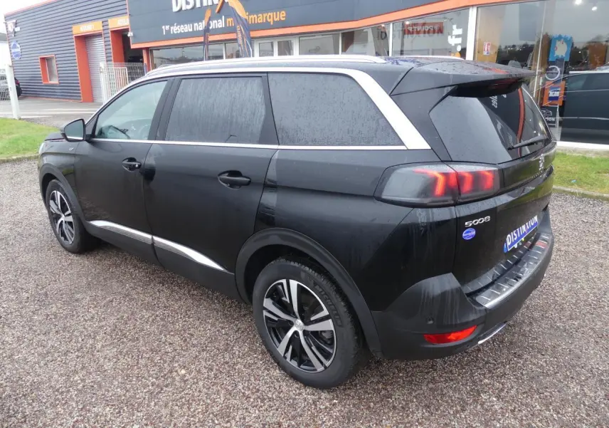 Peugeot 5008 GT noir métallisé vue 3/4 arrière droit, jantes bi-ton et barres de toit aluminium visibles.
