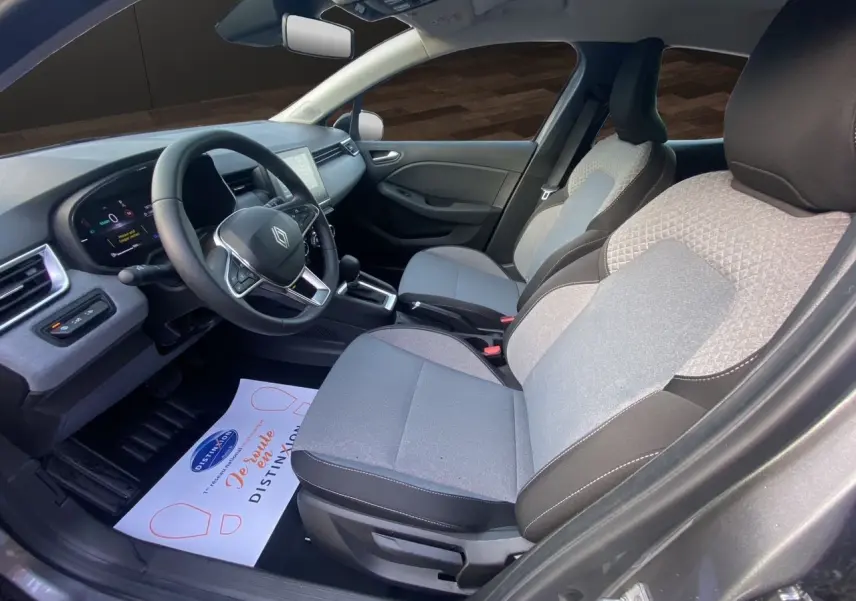 Vue intérieure côté conducteur de la Renault Clio V E-Tech gris schiste, avec sellerie textile gris à motif 3D et tableau de bord moderne.