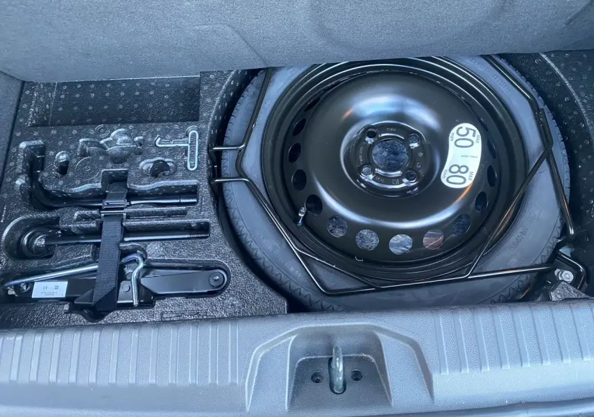 Vue plongeante sur la roue de secours temporaire noire et les outils de bord dans le coffre d'une Renault Clio V gris schiste.