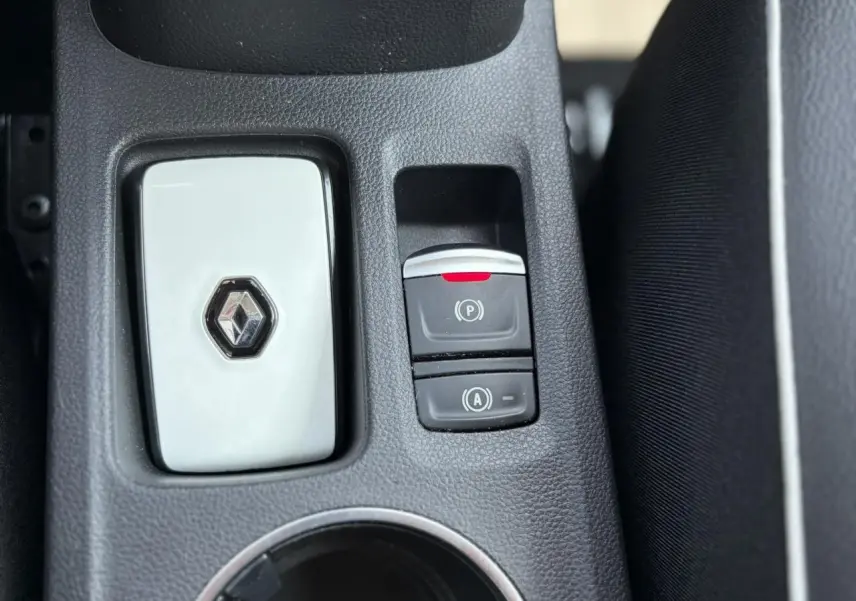 Gros plan sur la console centrale noire du Renault Captur 2024 avec bouton frein de parking électrique et logo Renault blanc.