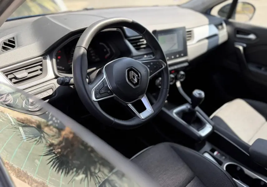 Vue intérieure côté conducteur du Renault Captur 2024, volant multifonction et écran tactile central visible.