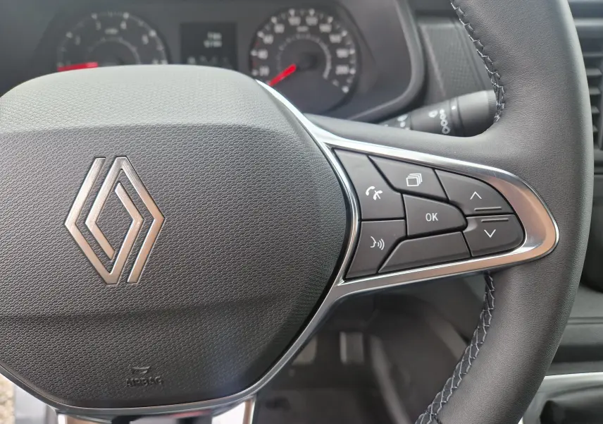 Gros plan sur le volant noir du Renault Trafic Fourgon 2025 avec commandes multifonctions à droite et logo central.