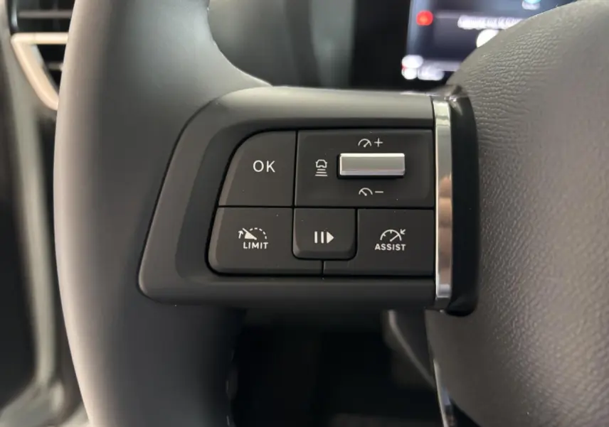 Gros plan sur les commandes au volant à gauche du Citroën C4 hybride 2026, volant cuir noir.