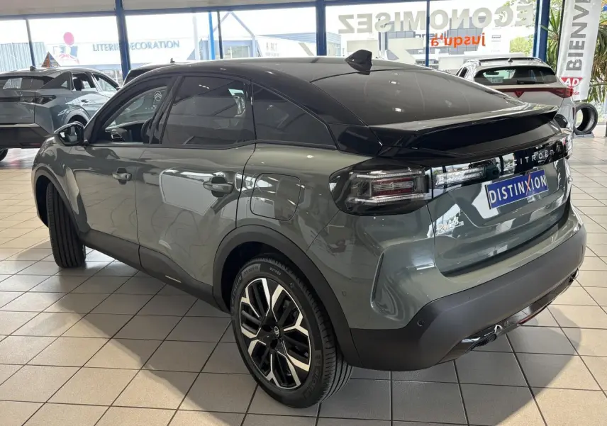 Vue 3/4 arrière droite d'une Citroën C4 hybride 2026 vert Manhattan avec toit noir et jantes alliage 18 pouces.