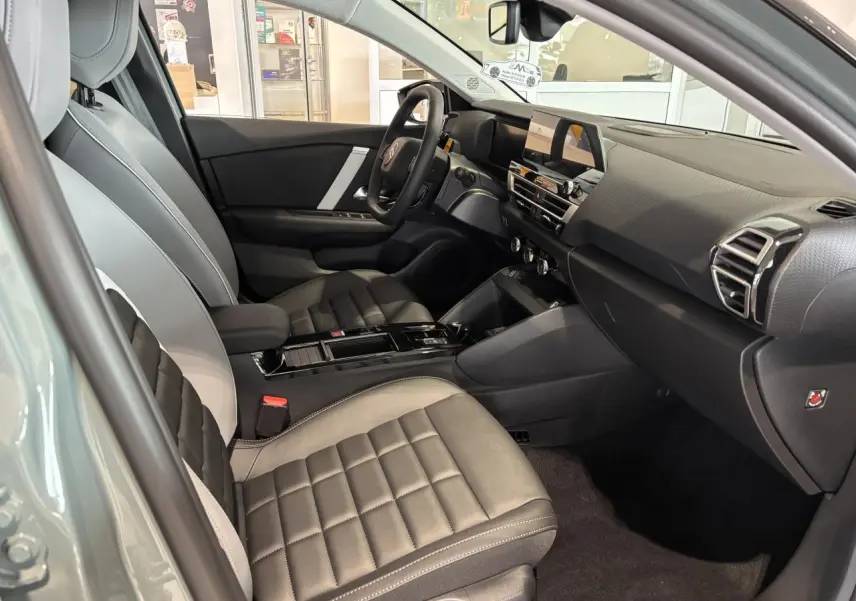 Intérieur avant droit de la Citroën C4 hybride 2026 avec sièges gris à surpiqûres et tableau de bord moderne noir.