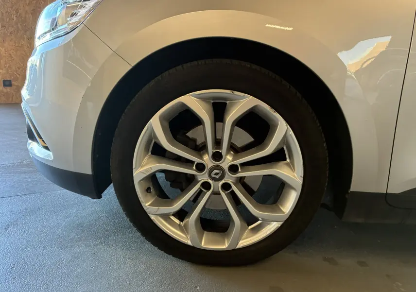 Vue de profil avant gauche d'un Renault Grand Scenic gris, mettant en valeur l'avant et la roue.
