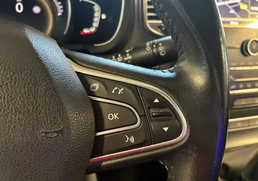 Gros plan sur les commandes du volant en cuir noir du Renault Grand Scenic gris, avec tableau de bord et écran GPS en arrière-plan.