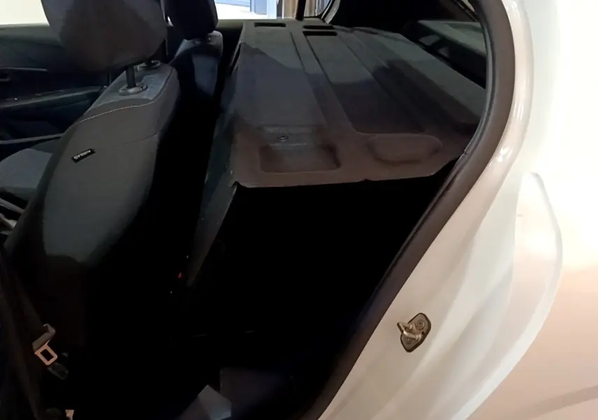Vue intérieure côté gauche du coffre ouvert d'une Peugeot 208 blanche, montrant la banquette arrière rabattue.