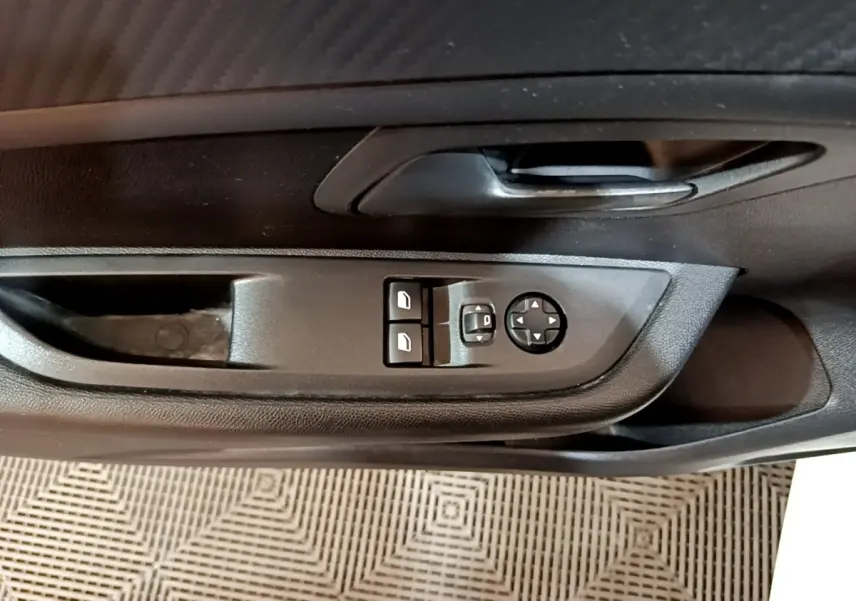 Vue rapprochée de la commande des vitres et rétroviseurs sur la porte intérieure noire d'une Peugeot 208 blanche.