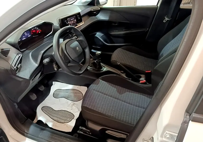 Vue intérieure côté conducteur de la Peugeot 208 blanche 2022, montrant le volant, tableau de bord digital et sièges tissu gris.
