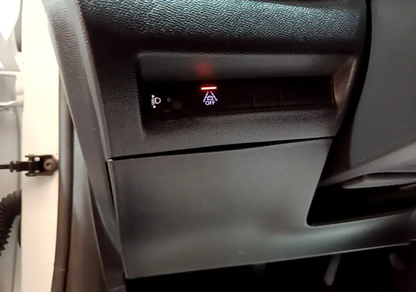 Gros plan sur les commandes sous le tableau de bord côté gauche d'une Peugeot 208 blanche, avec témoin d'alerte allumé.