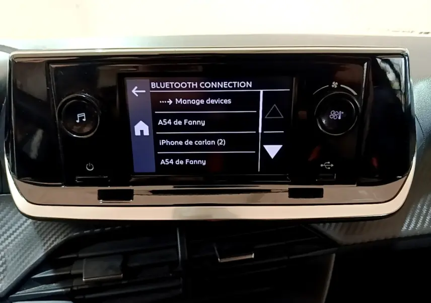 Écran tactile central noir affichant la connexion Bluetooth dans l'habitacle d'une Peugeot 208 blanche, vue de face.