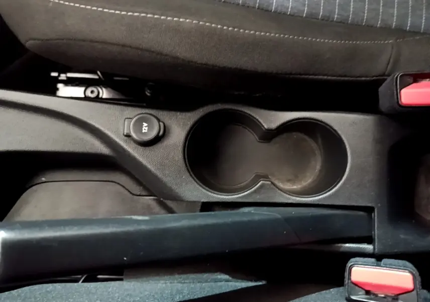 Vue rapprochée de la console centrale noire avec porte-gobelets et prise 12V dans une Peugeot 208 blanche.