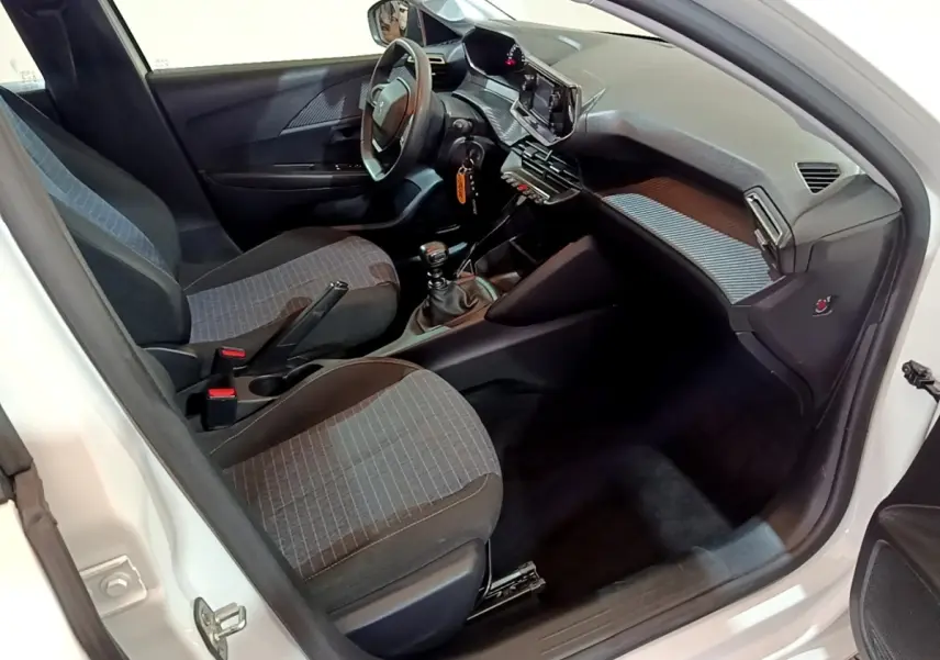 Intérieur avant droit d’une Peugeot 208 blanche 2022, montrant sièges tissu gris et tableau de bord avec écran tactile.