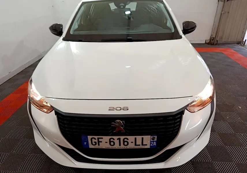 Vue avant rapprochée d’une Peugeot 208 blanche avec phares allumés dans un garage.