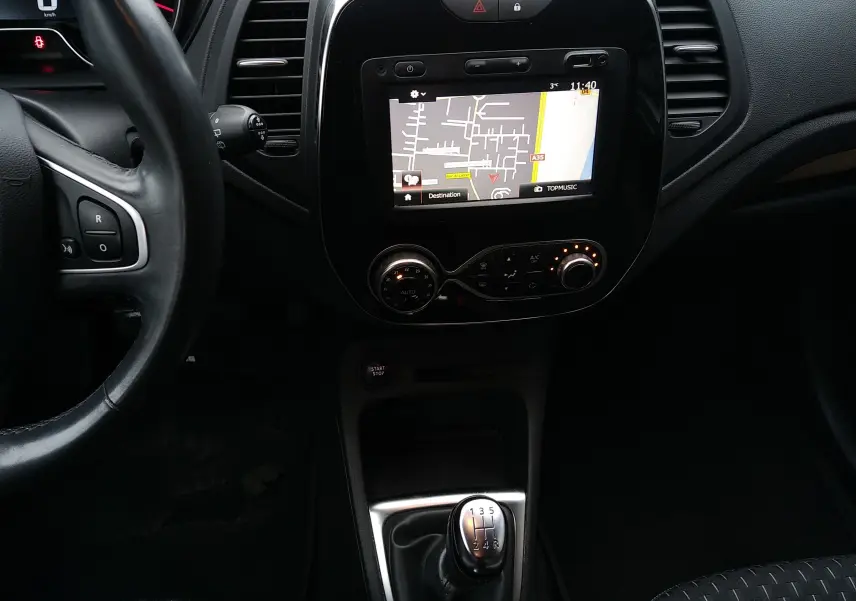 Vue intérieure centrée sur la console centrale et le levier de vitesse manuel du Renault Captur blanc avec écran GPS allumé.