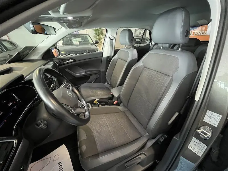 Vue intérieure côté conducteur du Volkswagen T-Cross 1.0 TSI 110 DSG Carat avec sièges gris en cuir et tissu, tableau de bord moderne.