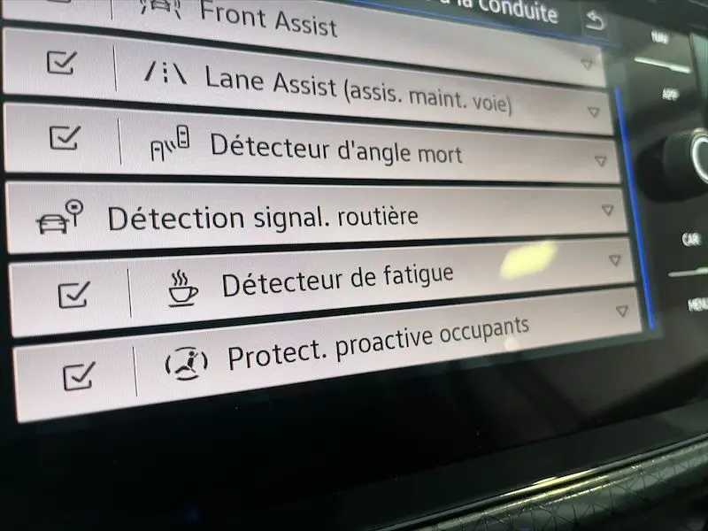 Écran tactile intérieur du Volkswagen T-Cross gris Limestone, affichant les options d’aide à la conduite activées.