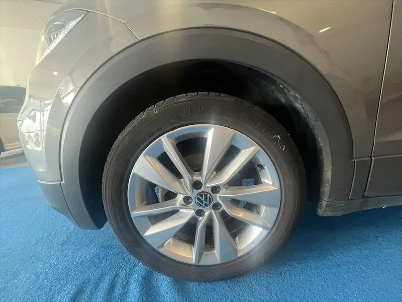 Gros plan sur la roue avant gauche d'un Volkswagen T-Cross gris Limestone métallisé, soulignant la jante alliage et le pneu.