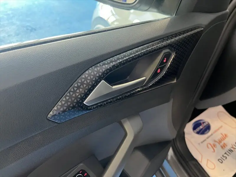 Poignée intérieure côté conducteur du Volkswagen T-Cross gris Limestone, avec motifs triangulaires et commandes de verrouillage.
