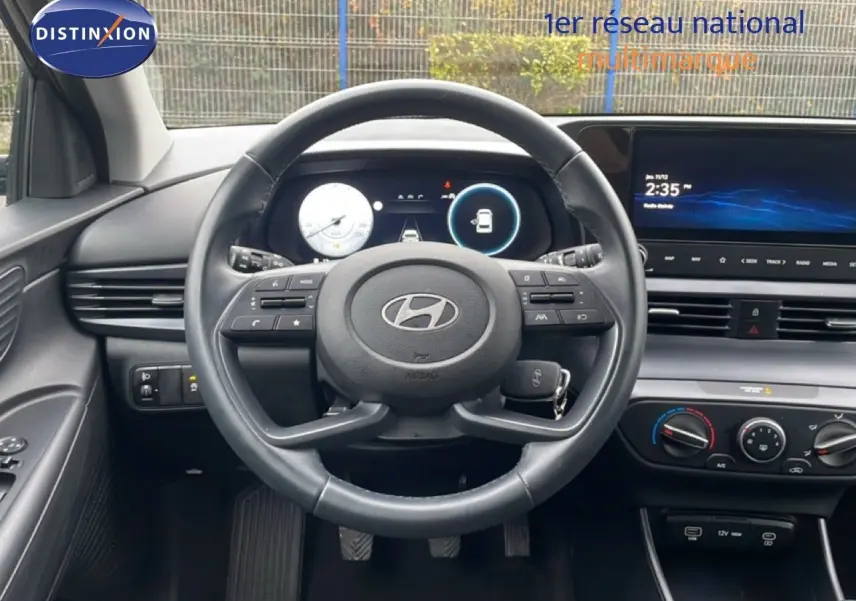 Vue intérieure centrée sur le volant cuir noir d’une Hyundai i20 2025, avec tableau de bord numérique et écran tactile.
