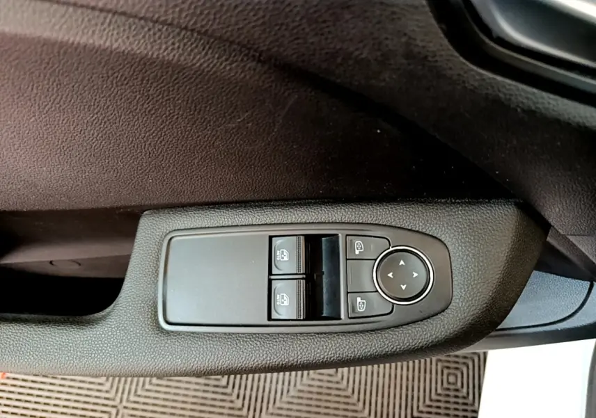 Détail des commandes de lève-vitres et rétroviseurs sur la porte côté conducteur d'une Renault Clio blanche.