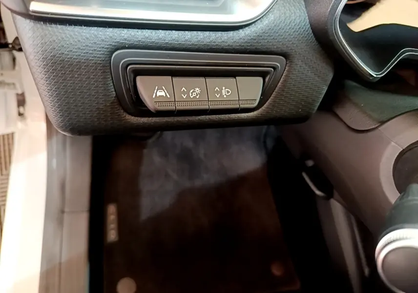 Gros plan sur les commandes de réglage d'assistance et éclairage côté gauche du tableau de bord d'une Renault Clio blanche.