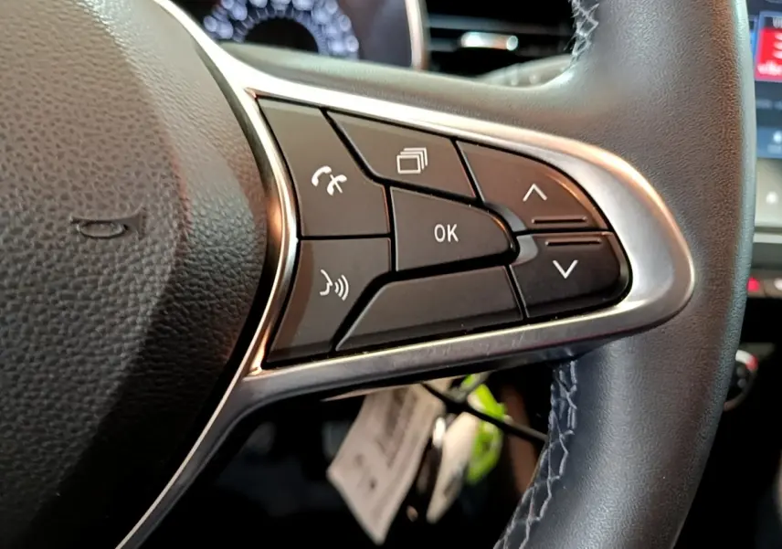 Gros plan sur les commandes multifonctions à droite du volant cuir noir de la Renault Clio Business blanche de 2021.