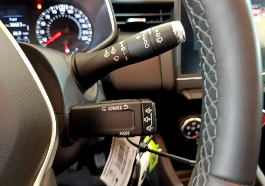 Gros plan sur la commande multifonction et le volant cuir de la Renault Clio Business blanche, tableau de bord en arrière-plan flou.