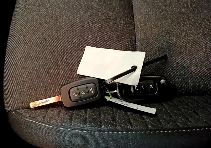 Clé de voiture Renault Clio Business blanche posée sur un siège tissu gris foncé, vue rapprochée.