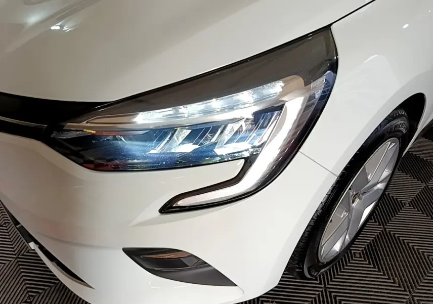 Gros plan sur l'avant droit blanc d'une Renault Clio 2021, mettant en valeur le phare LED et la jante alu.