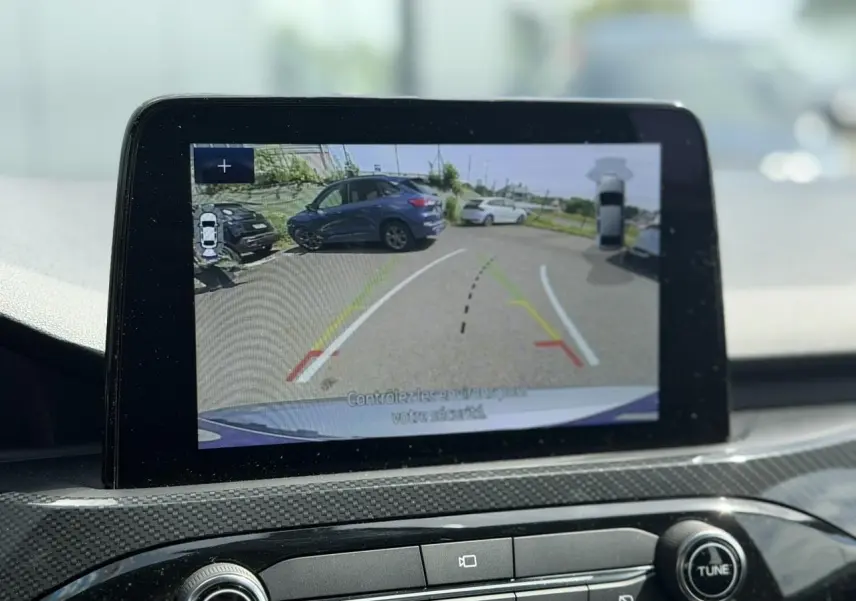 Écran intérieur montrant la caméra de recul avec vue arrière sur un Ford Kuga gris Solar en stationnement.