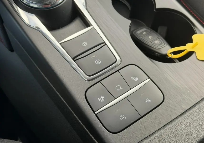 Vue rapprochée de la console centrale du Ford Kuga 2024 gris Solar, avec boutons de contrôle et clé dans porte-gobelets.