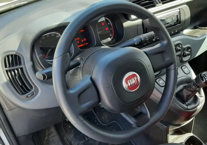 Vue intérieure centrée sur le volant noir FIAT et le tableau de bord de la Fiat Panda blanche de 2018 avec levier de vitesse manuel.