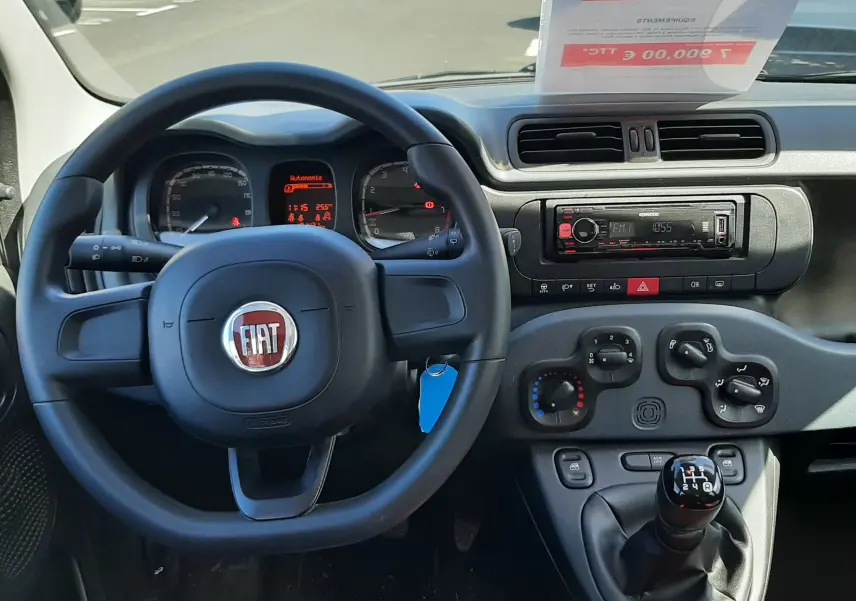 Vue intérieure avant centrée sur le volant Fiat Panda blanc 2018 avec tableau de bord, commandes manuelles et levier de vitesses.
