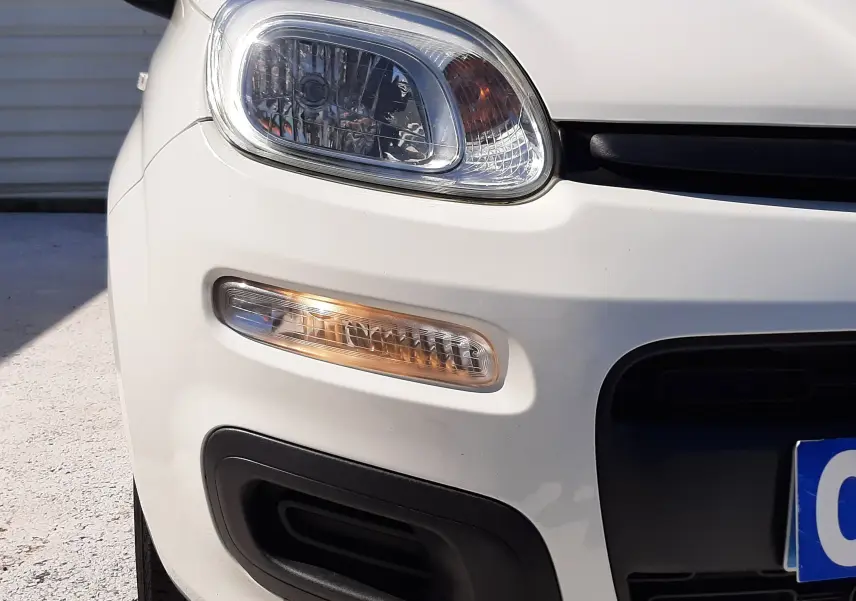 Gros plan sur l'avant gauche d'une Fiat Panda blanche 2018, mettant en valeur le phare et le clignotant.