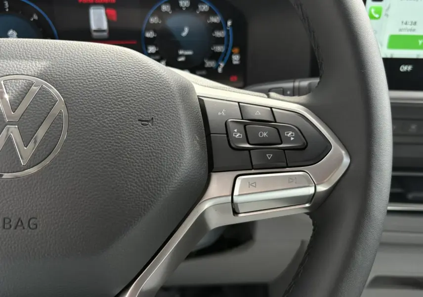 Gros plan sur le volant multifonction noir du Volkswagen Transporter T7 avec commandes intégrées et tableau de bord numérique en arrière-plan.