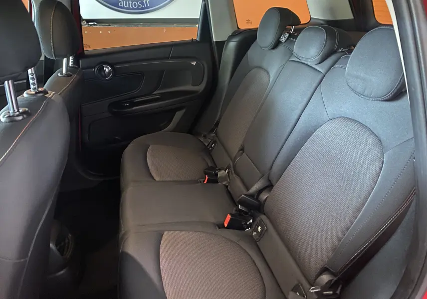 Vue intérieure montrant les sièges arrière en tissu noir d'une MINI Countryman rouge toit noir, avec appuie-têtes et ceintures visibles.