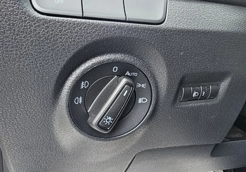 Gros plan sur le bouton de commande des phares dans l'habitacle noir d'une Skoda Fabia blanche côté gauche.