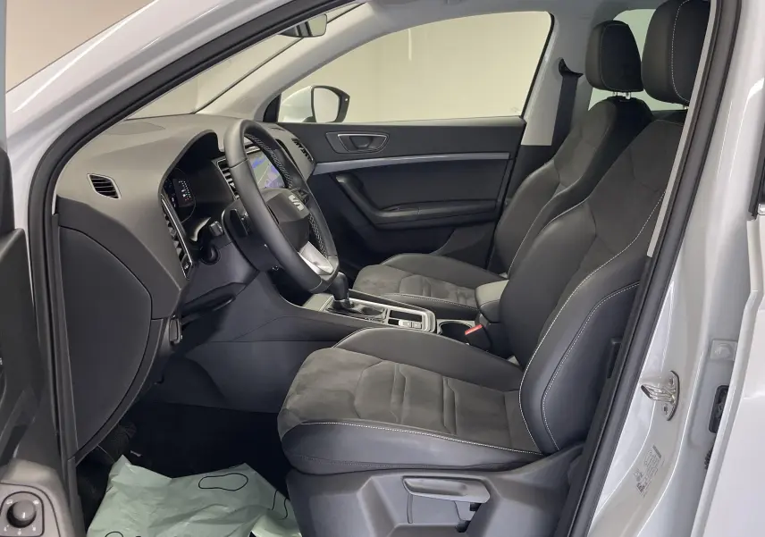 Vue côté conducteur de l'intérieur du SEAT Ateca blanc Nevada 2024, avec sièges noirs et tableau de bord moderne.