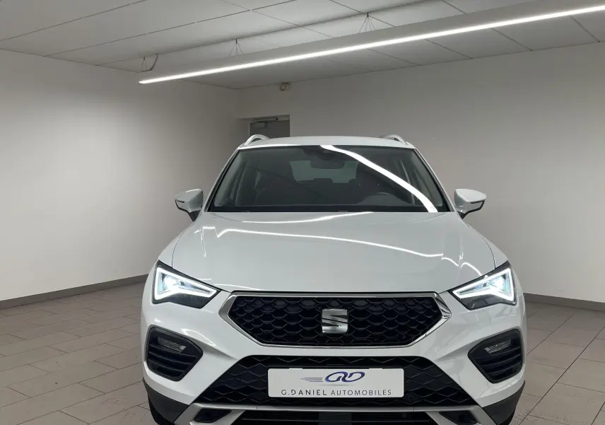 Vue avant d'un SEAT Ateca blanc Nevada 2024 avec phares LED allumés et calandre hexagonale noire.