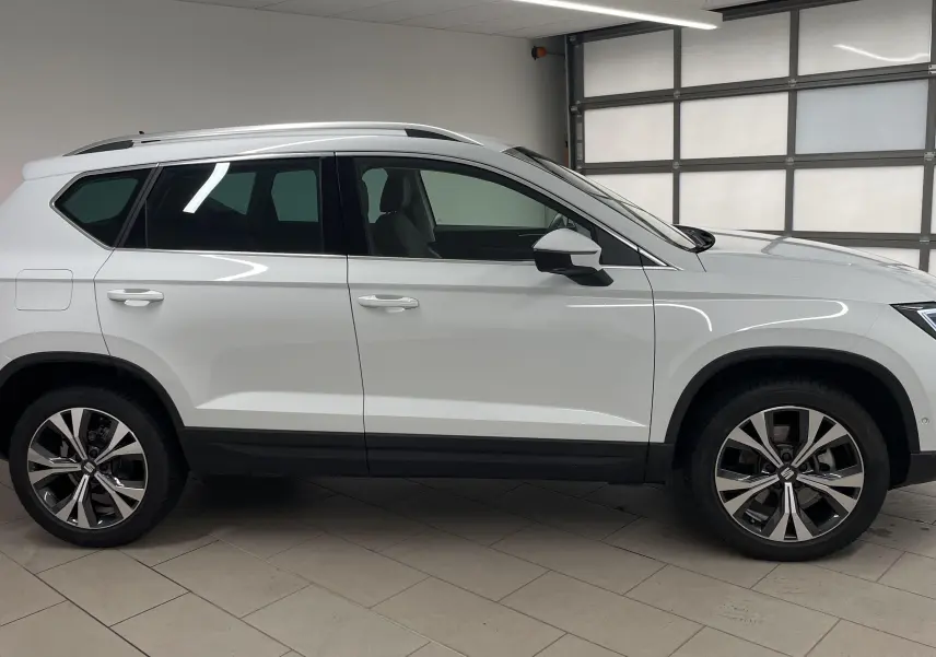Profil côté gauche du SUV SEAT Ateca blanc Nevada 2024 avec jantes alliage 18'' et hayon électrique en intérieur showroom.