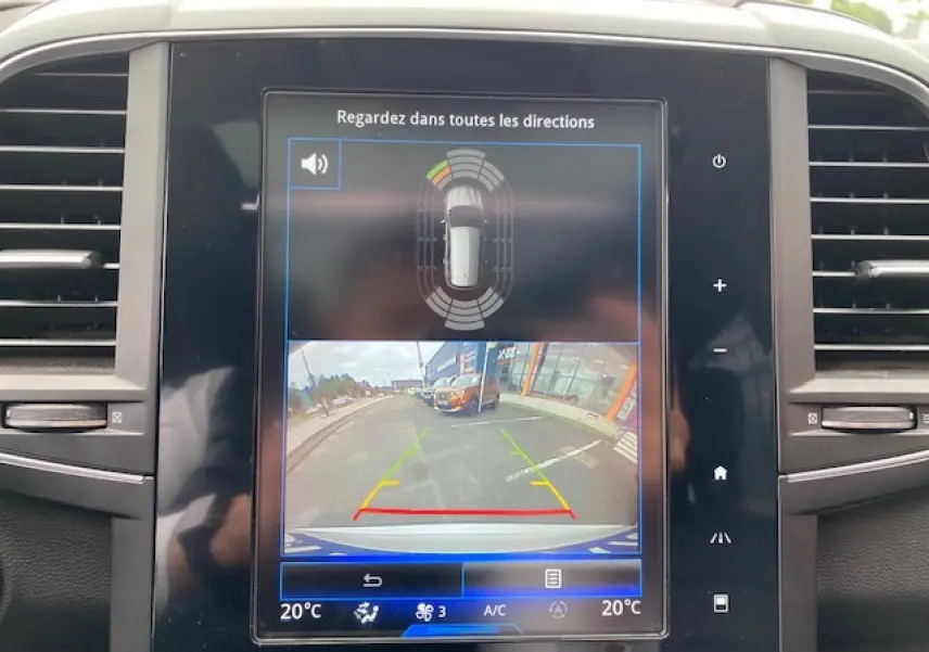 Écran central du Renault Koleos 2019 blanc montrant la caméra de recul et les capteurs de stationnement.