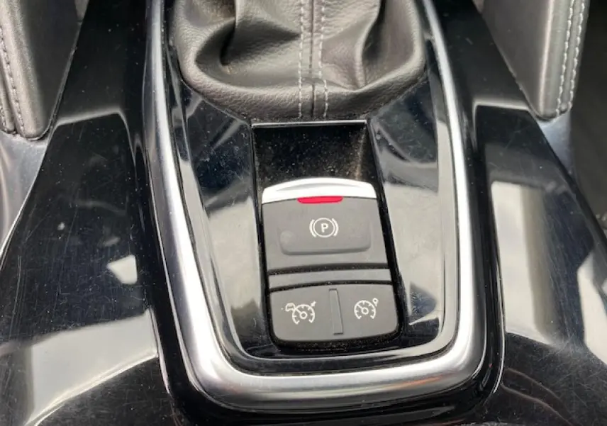 Gros plan sur la console centrale noire du Renault Koleos blanc 2019, montrant le frein à main électronique et commandes de régulateur.