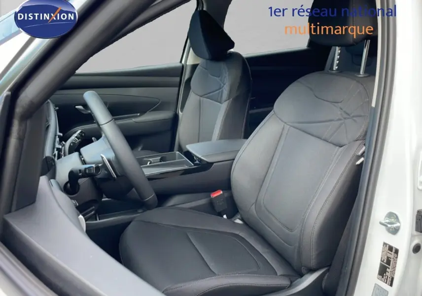 Vue intérieure côté conducteur du Hyundai Tucson blanc Atlas 2026, sièges tissu noir et volant multifonction.