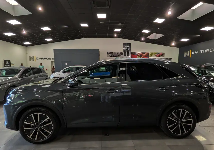 Vue latérale droite d'un DS7 gris 2024 avec jantes bi-ton et vitres teintées en showroom intérieur.