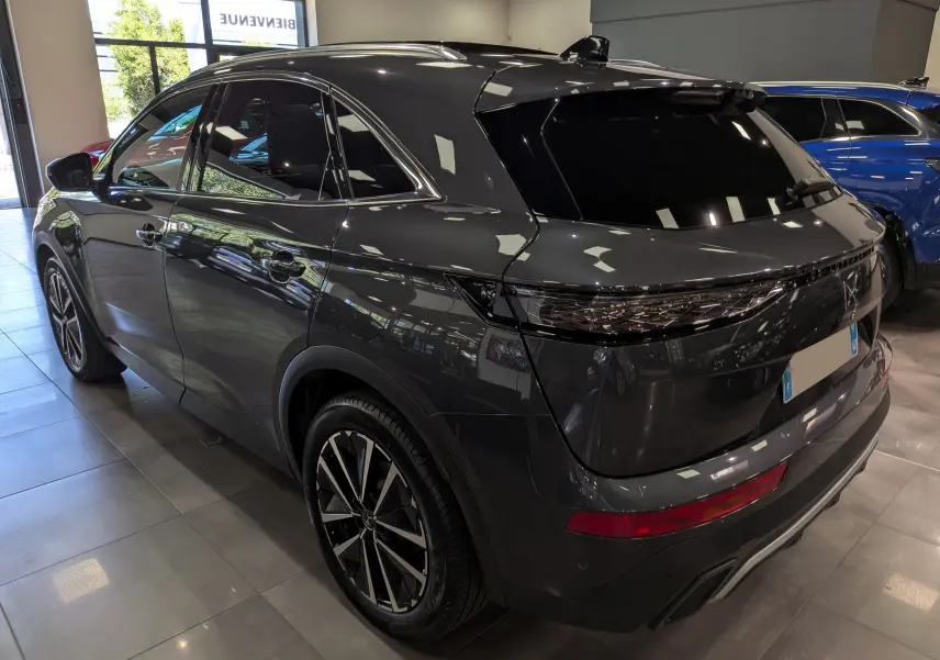 DS7 BlueHDi 130 gris 3/4 arrière droit en showroom, avec jantes bi-ton et feux arrière étirés noirs.