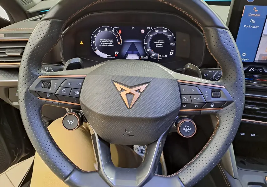 Vue rapprochée du volant perforé avec logo cuivré du CUPRA Leon 2025, tableau de bord digital et commandes intégrées.